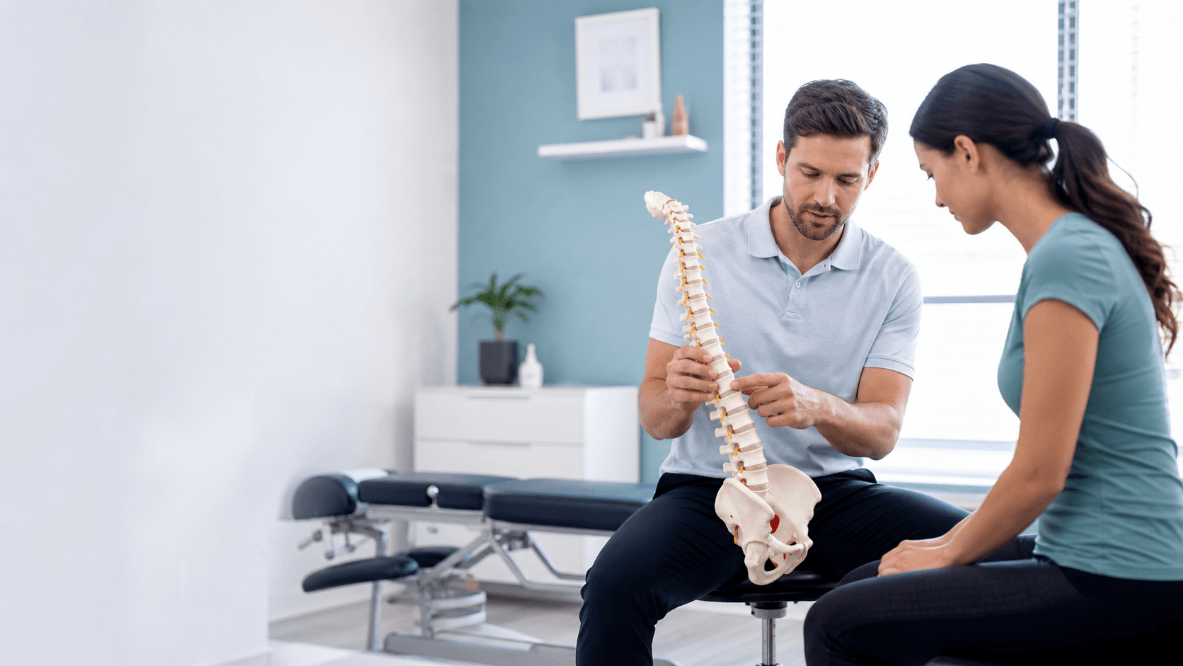 Clinician reviewing a spine model with a patient in a bright consultation room